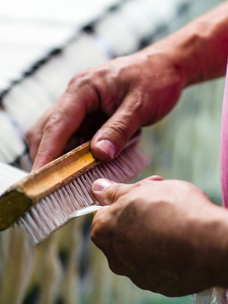 Deux mains passent une brosse sur une nappe de fils tendus